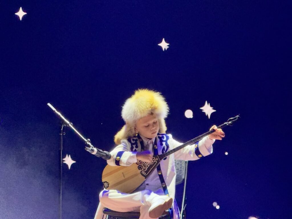 A performer in a flowing red and white costume dancing on stage with a pyramid and desert backdrop at Symphony of the Earth